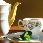 a tea pot, cup and saucer with mint leaves on the saucer