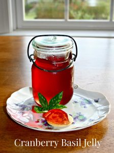 a jar of cranberry basil jelly on a plate with blue flowers and a cracker with jelly shaped like a strawberry