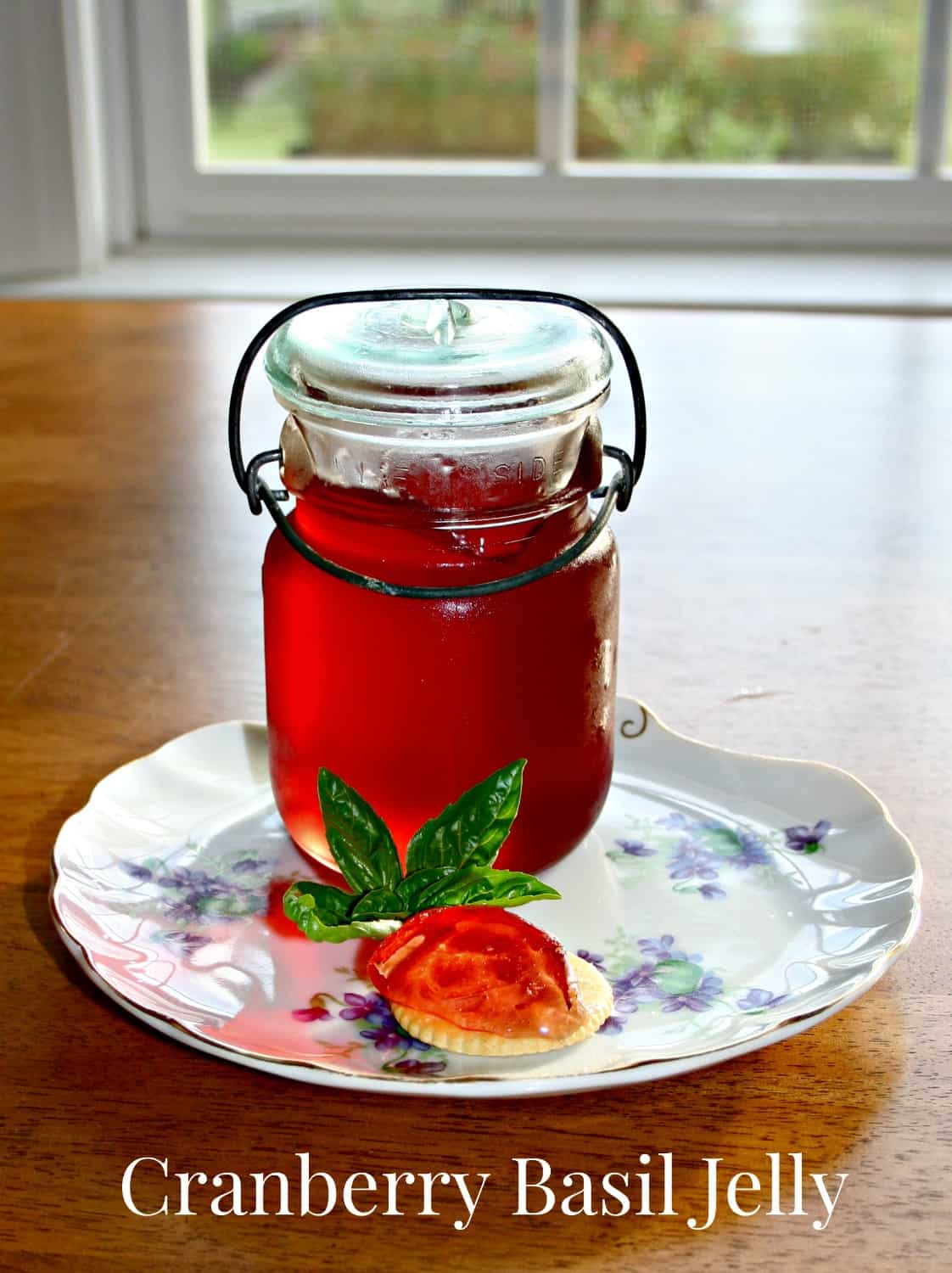a jar of cranberry basil jelly on a plate with blue flowers and a cracker with jelly shaped like a strawberry