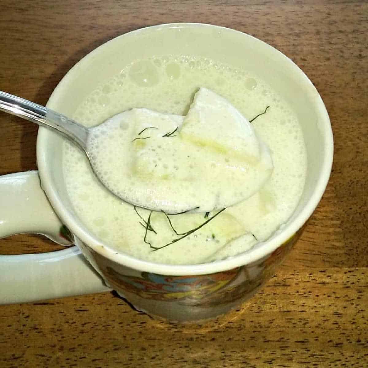a spoon dipped in a mug of cucumber soup