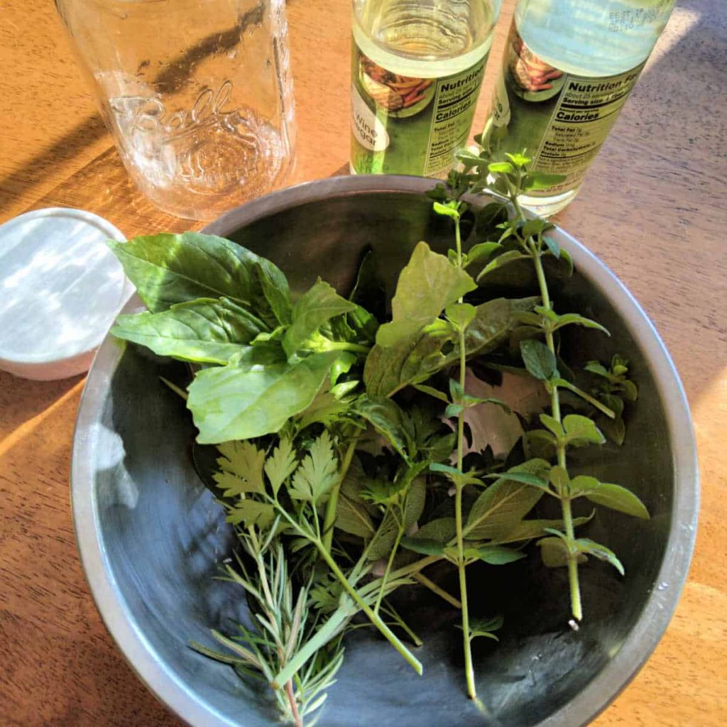 herbs in a metal bowl, glass jar, and wine vinegar