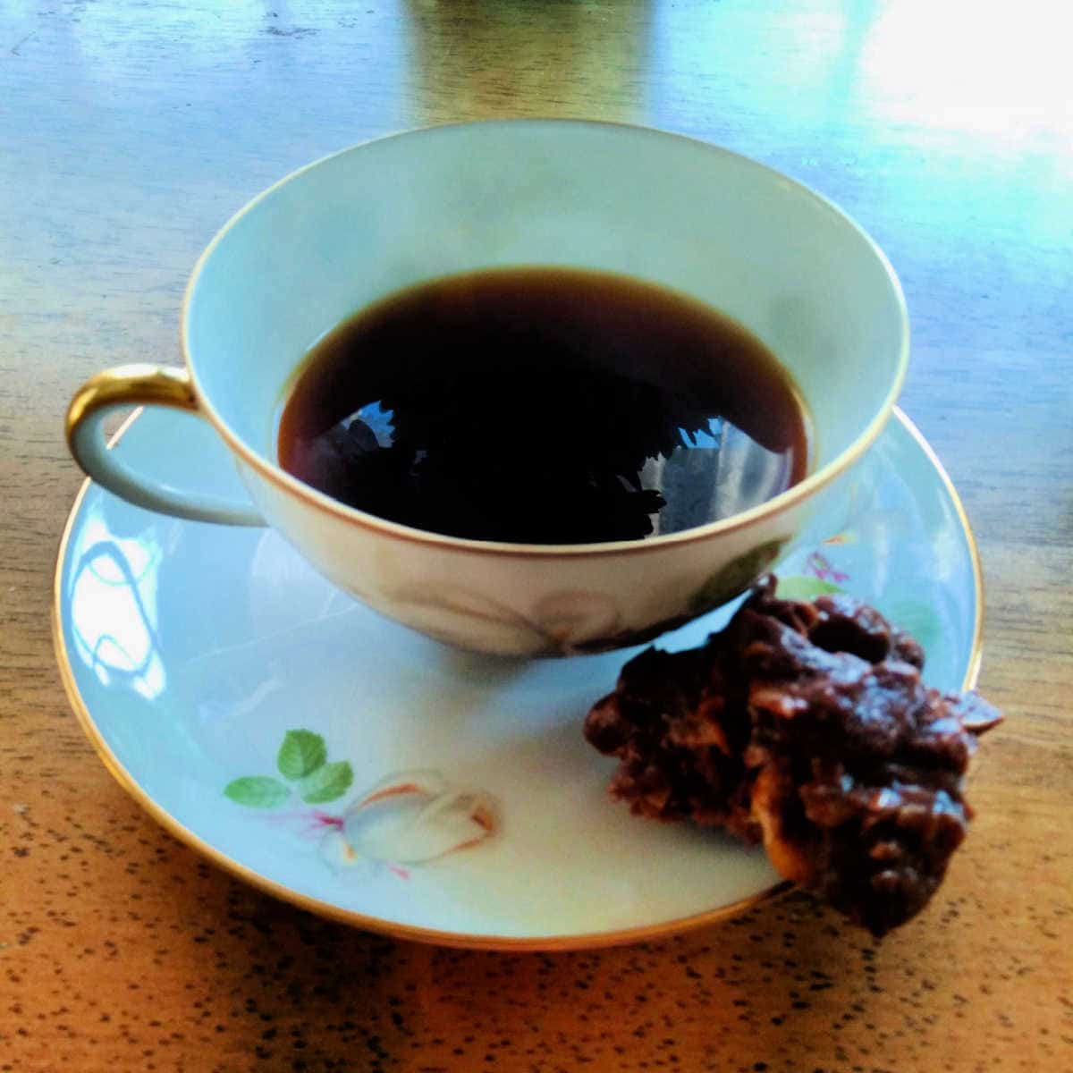 a chocolate peanut cluster cookie on a saucer with a cup of coffee