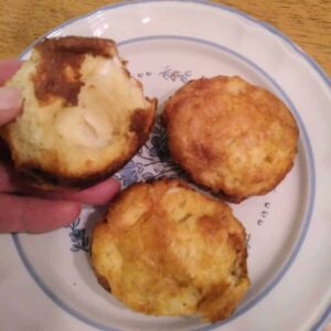 a woman holding a popover with the cream interior revealed and two other popovers on a plate