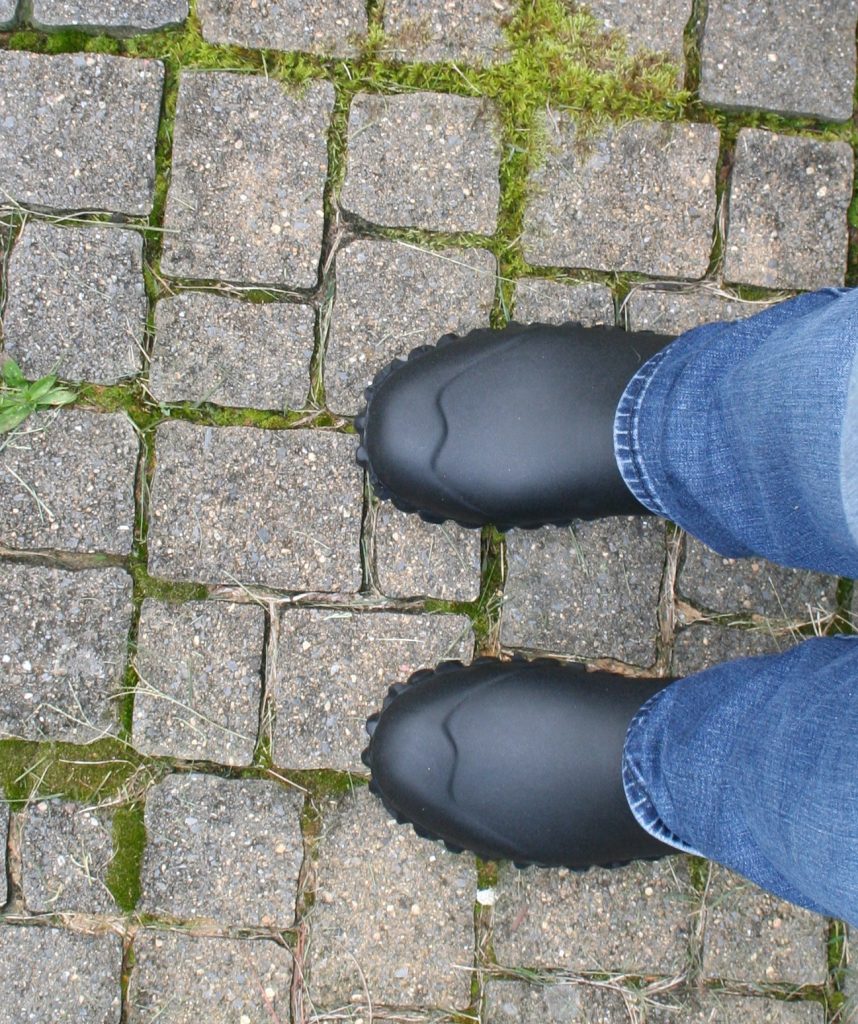 looking down at a pair of black boots standing on cobblestones.