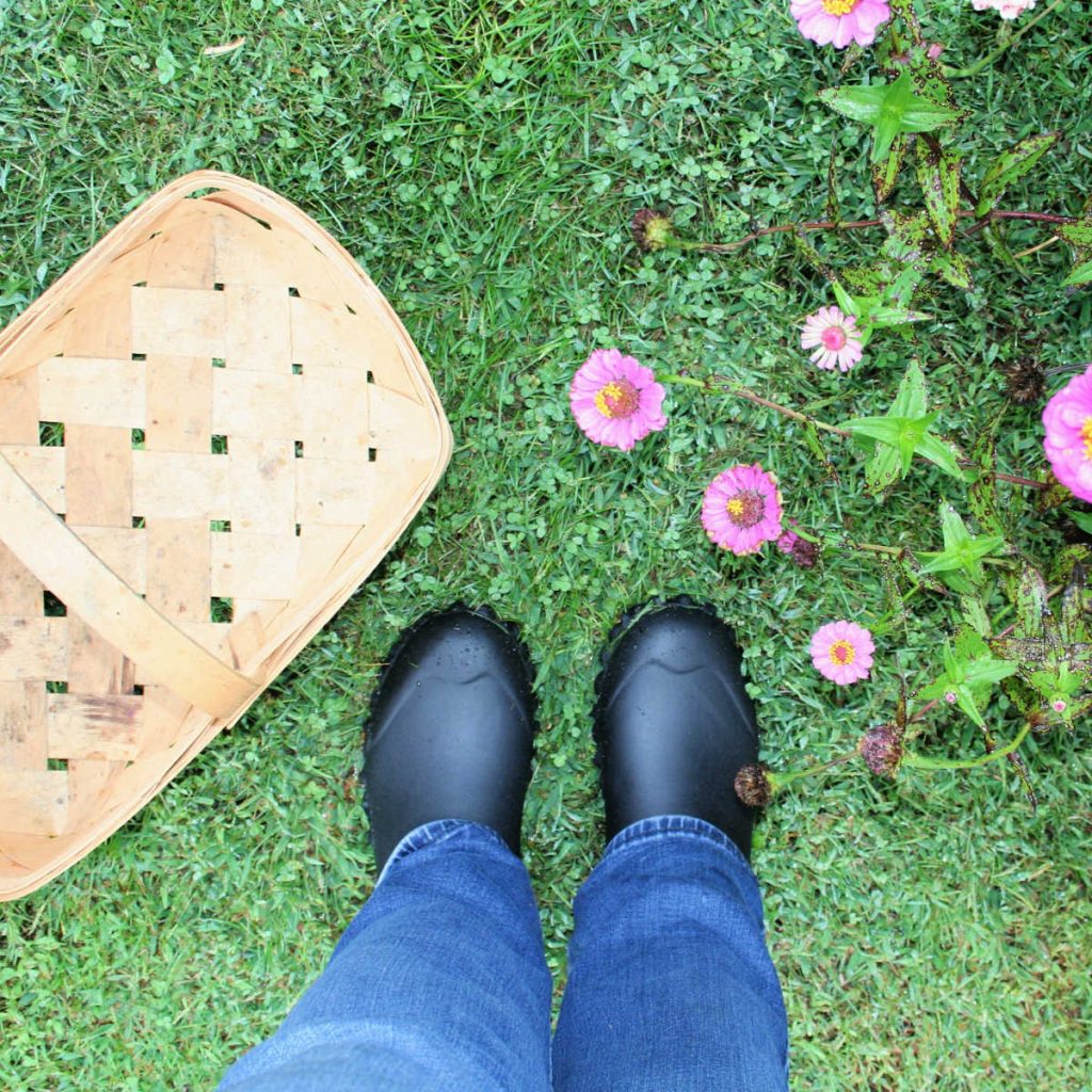 looking down at a woman's feet in black Hisea boots with a basket and flowers on the lawn