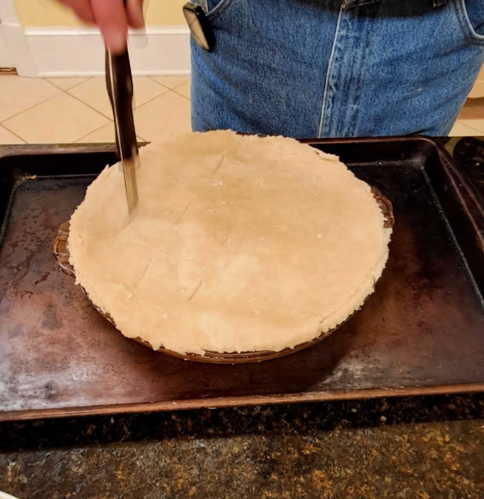 a man cutting slits in the top of a pie crust before baking