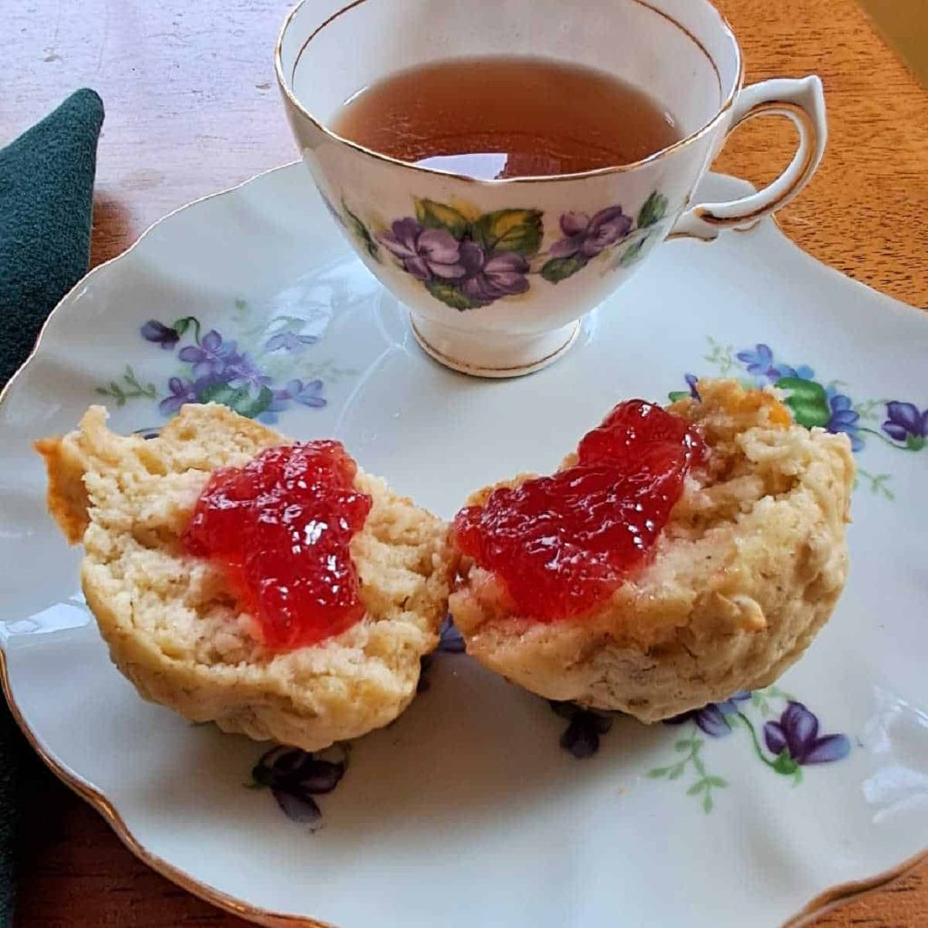 oatmeal muffins spread with strawberry jelly on a fancy plate with a cup of tea